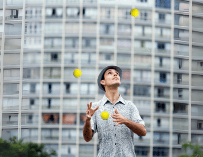 Mann jongliert konzentriert Bälle vor einem Bürogebäude